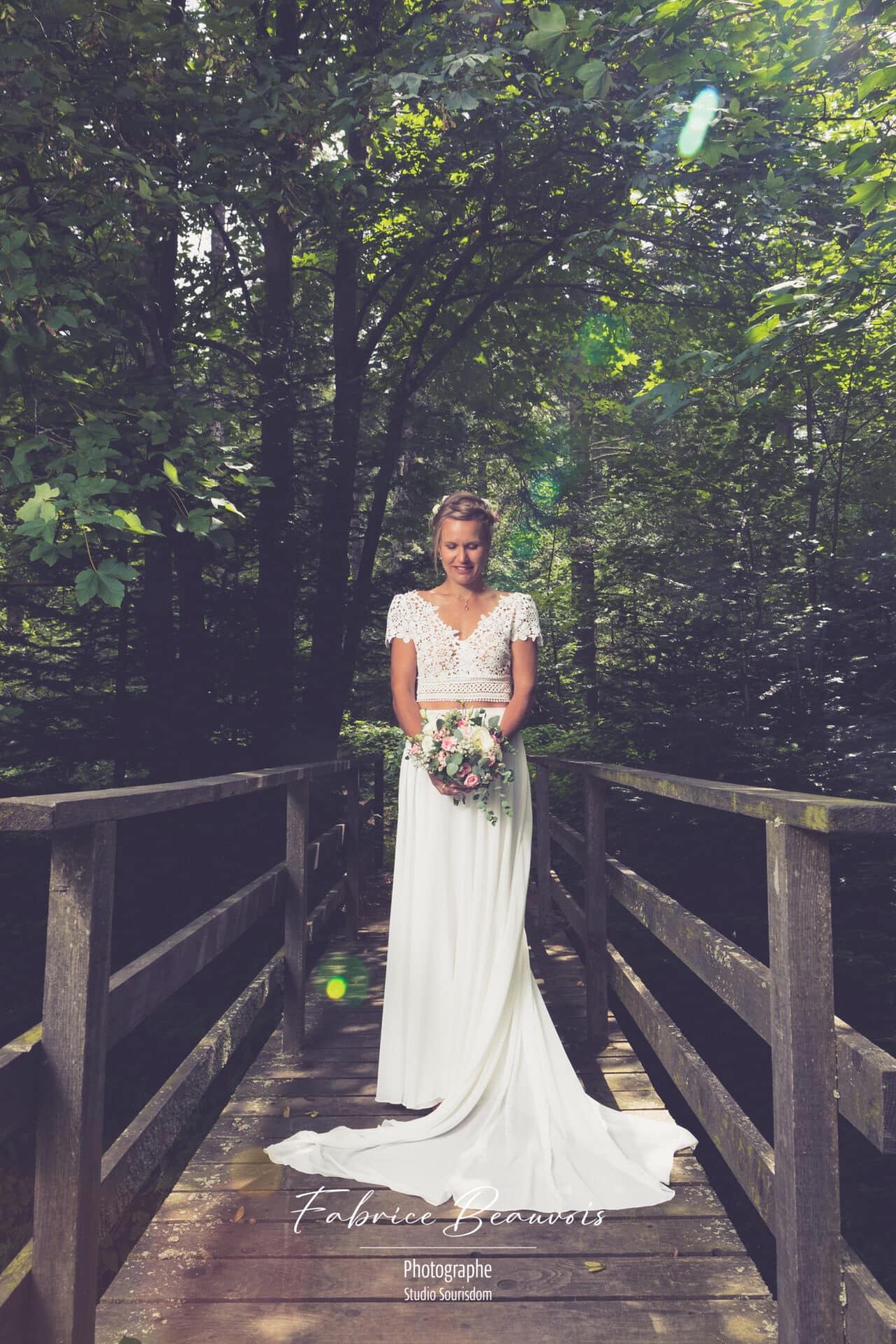 La mariée pose avec candeur sur un petit pont en bois ensoleillé